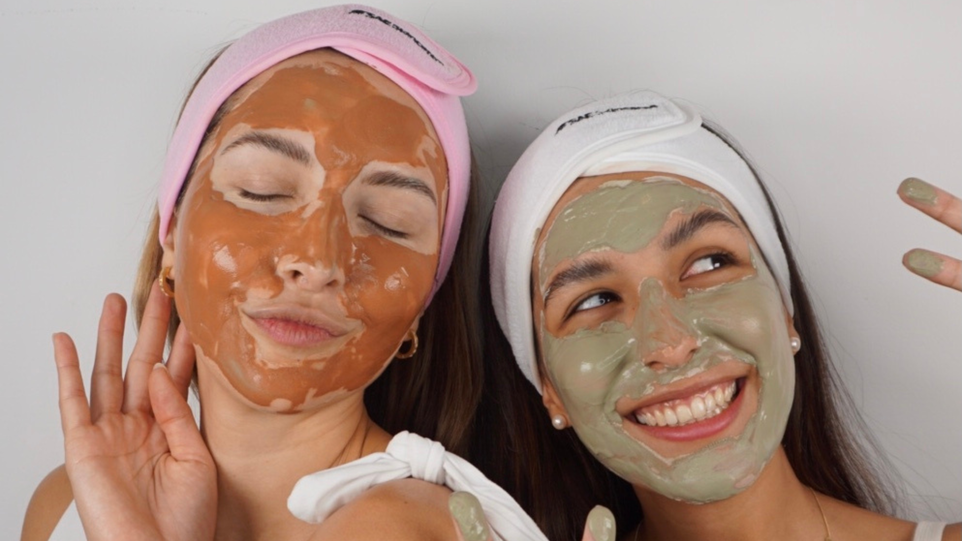 Two women applying facial masks with a neutral background
