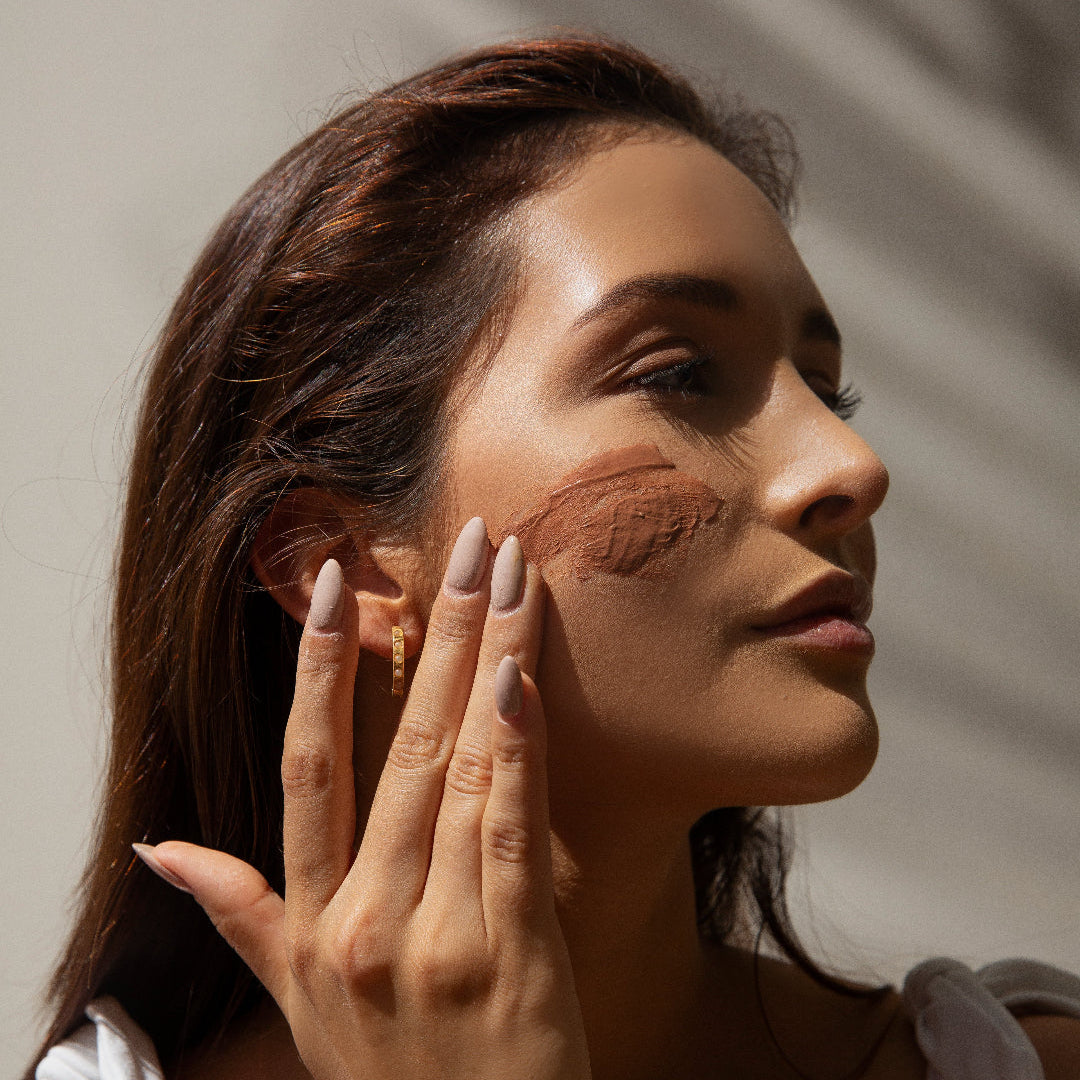 Woman applying makeup with a brush on her face against a neutral background